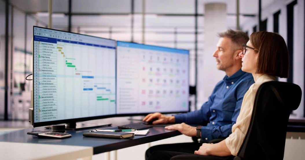 Two business owners sit in front of two large monitors displaying attendance data.