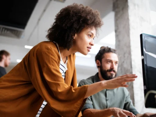 A manager discusses a project with an employee at their desk.